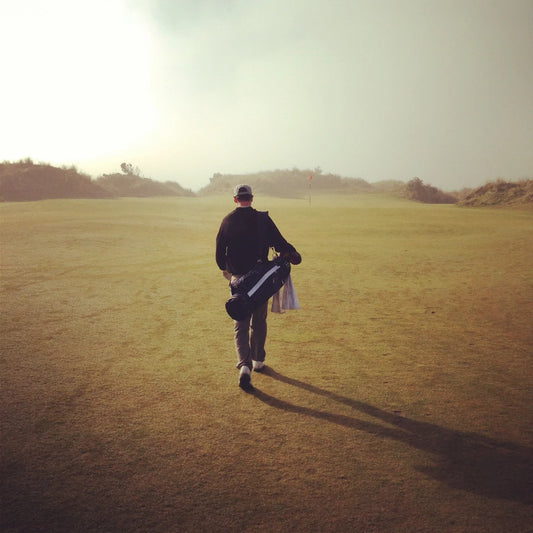 Golfare ryggtavla går bortåt på en solig golfbana med en golfbag på axeln