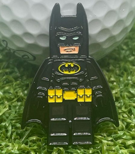 Golfmarkör liknade en lego Batman, lutad mot en vit golfboll.