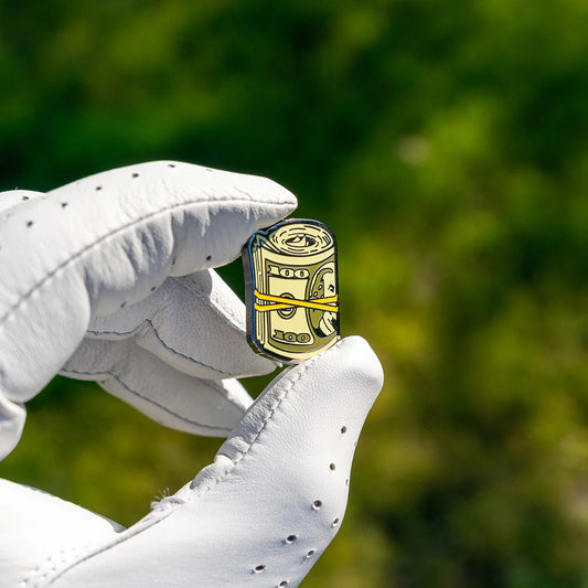 En golfhandske sm håller upp en golfbollmarkör som liknar pengar.