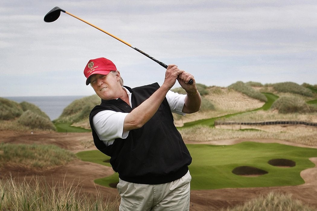 Donald Trump spelar golf, han har en röd keps och en svart pullover på sig.