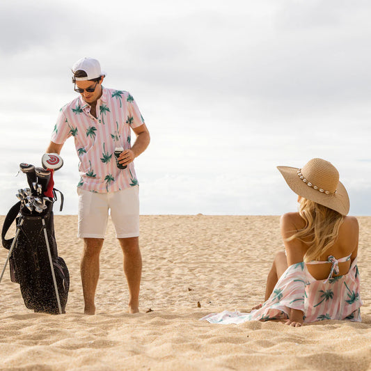 Två personer befinner sig på en strand, mannen på bilden har golfkläder på sig och en golfbag med sig på stranden.